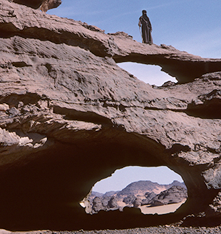 Ein Felsbogen erhebt sich mächtig aus dem schwarzen Gestein, Akakus-Massiv in Südlibyen